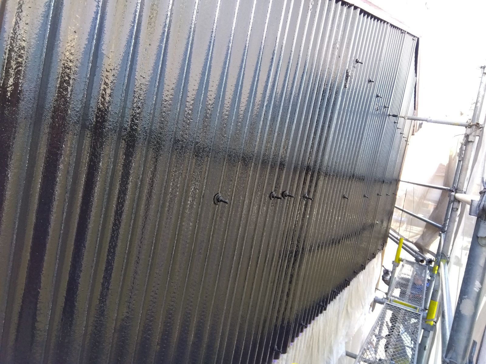 65915f54-488b-4367-a02f-7394803110a4 | 岐阜県大垣市 塗りかえ工房 Corrugated vertical metal wall with evenly spaced bolts; scaffolding is visible on the right at a construction site.