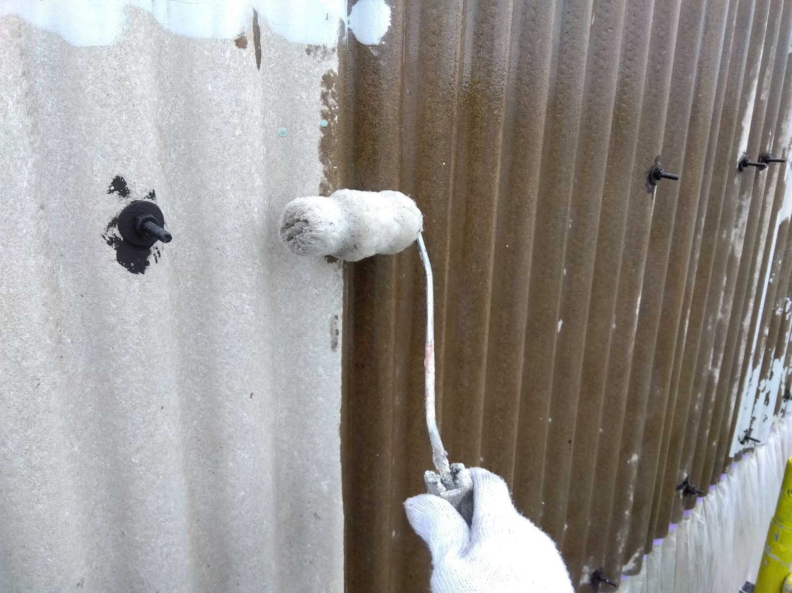 bb65b508-9adf-4dbe-ab8d-0d05c52af2cf | 岐阜県大垣市 塗りかえ工房 Person wearing gloves using a paint roller to apply white paint on a textured wall exterior surface