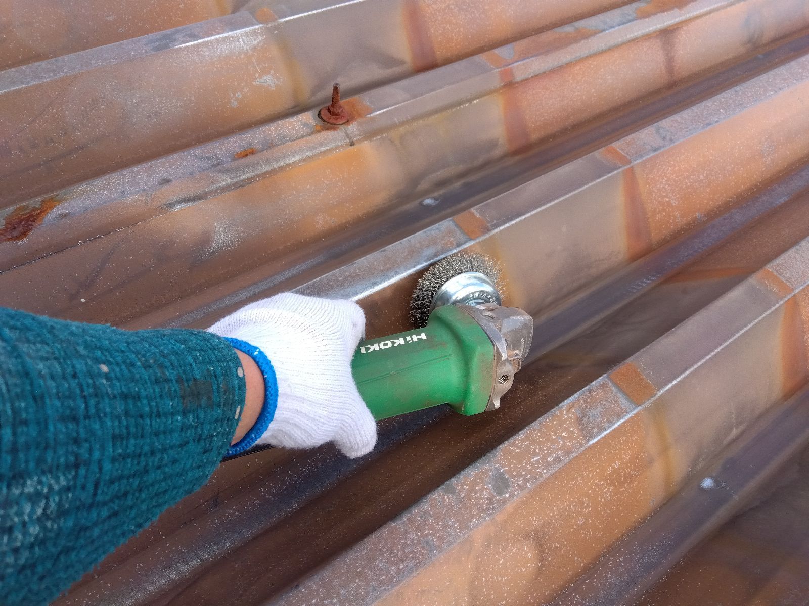 c79e04d0-e25b-4242-9e0c-839cff12fe6a | 岐阜県大垣市 塗りかえ工房 Worker wearing white glove polishes rust on metal surface with a green rotary tool (grinder) and wire brush attachment