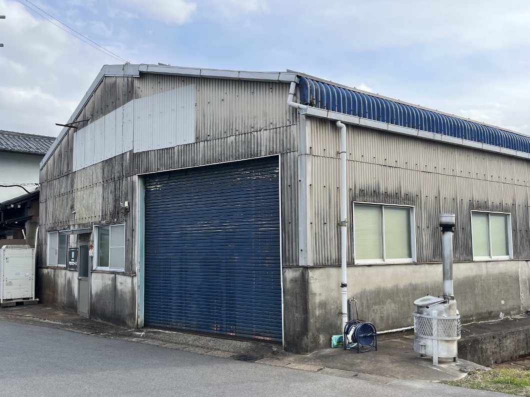 20250322マツバラワーク1-1 1280x960 | 岐阜県大垣市 塗りかえ工房 Industrial metal warehouse with a large blue roll-up door and weathered siding on a quiet street.