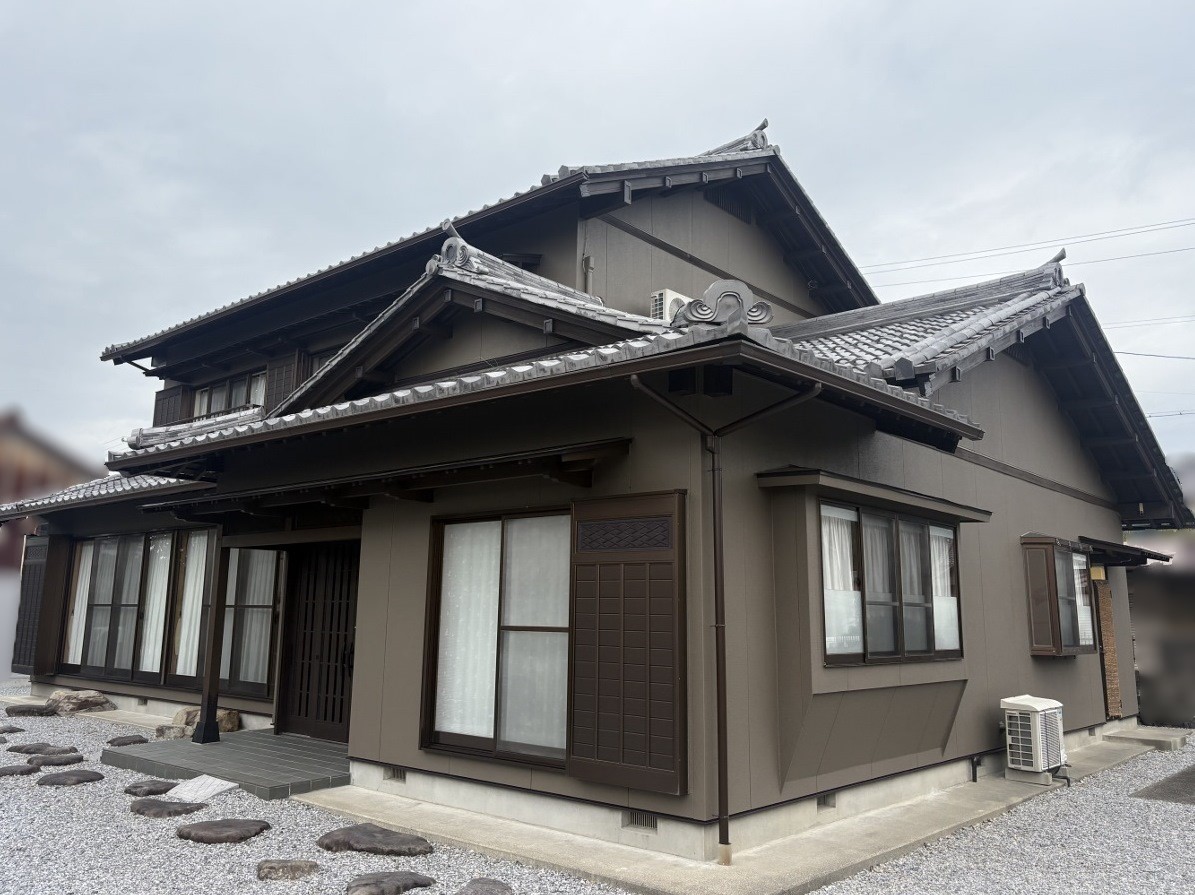 Traditional Japanese house with a dark brown exterior and layered tiled roof, front entrance visible.