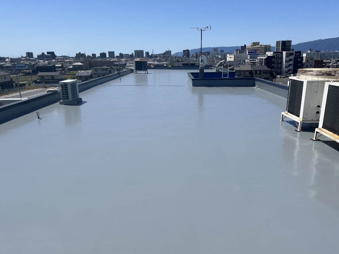 Flat rooftop with a light gray waterproof coating, several HVAC units and a satellite dish, city skyline in the distance on a clear sunny day.